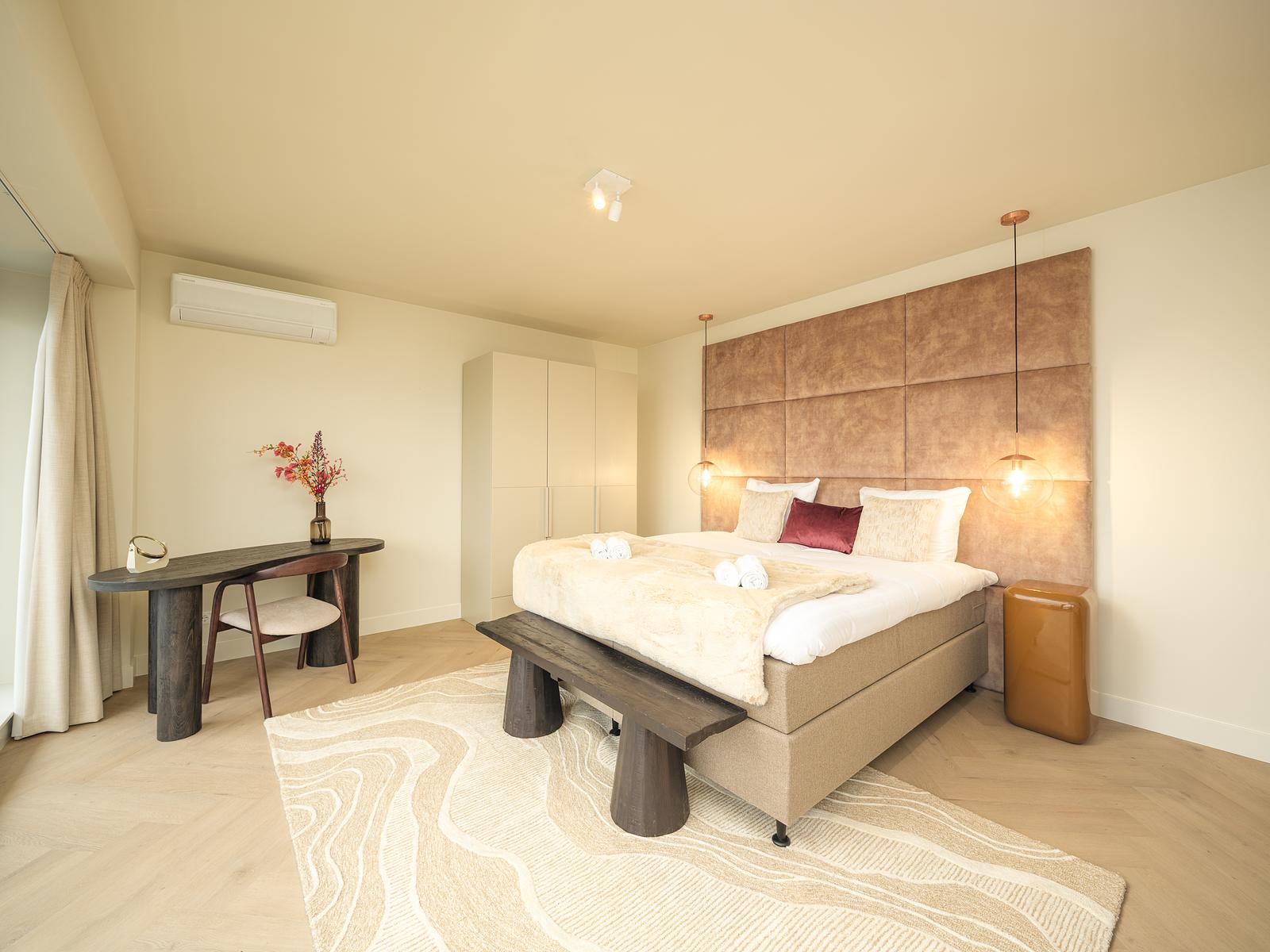 A spacious bedroom with a velvet headboard, glowing pendant lights and a soft throw on the bed